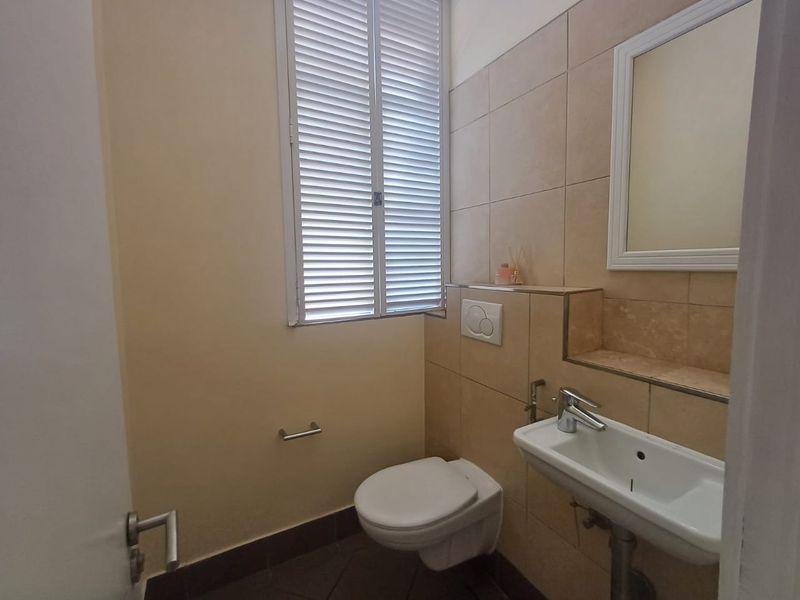 A clean and functional guest bathroom featuring a wall-mounted toilet, basin, and tiled wall finishes with a shuttered window.