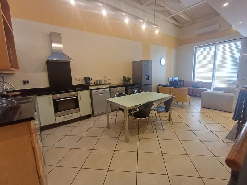 Spacious open-plan living area featuring a functional kitchen with built-in appliances, tiled flooring, and high ceilings with exposed rafters.