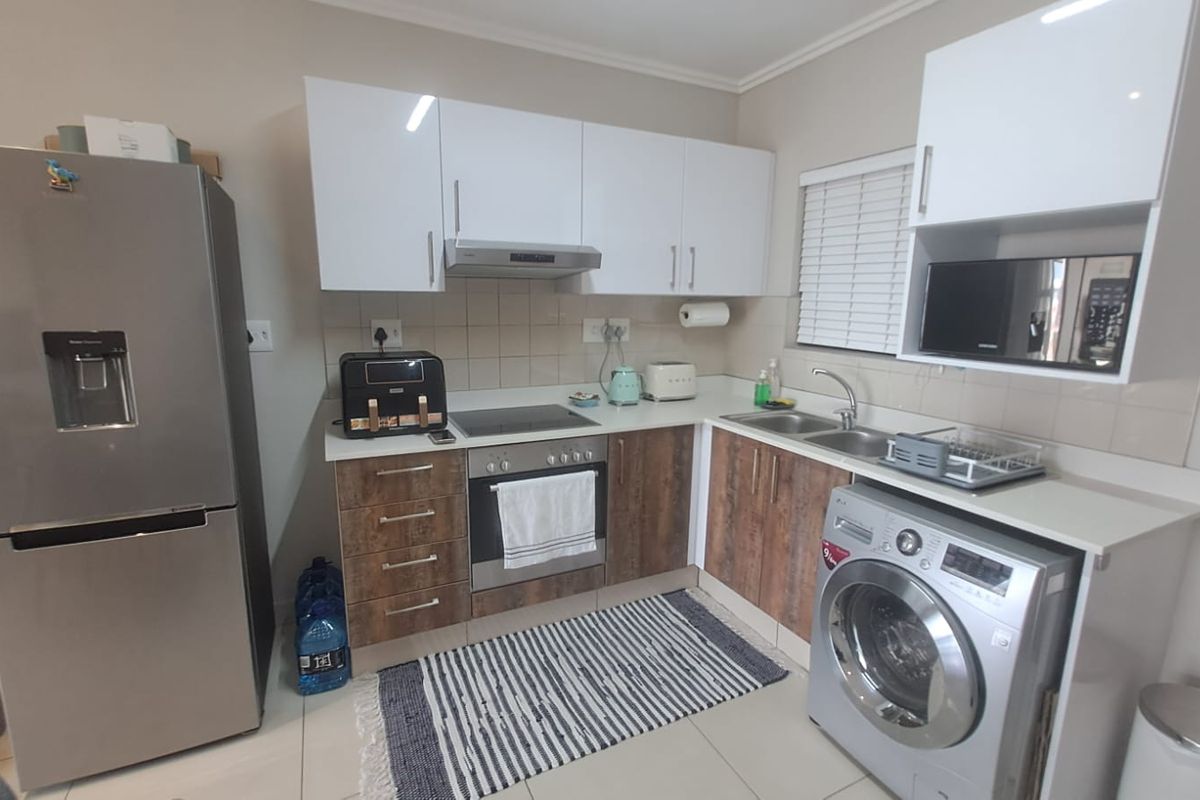 A functional kitchen featuring white upper cabinets, wood-finish lower cabinetry, integrated oven and hob, and a tiled backsplash with a double sink.