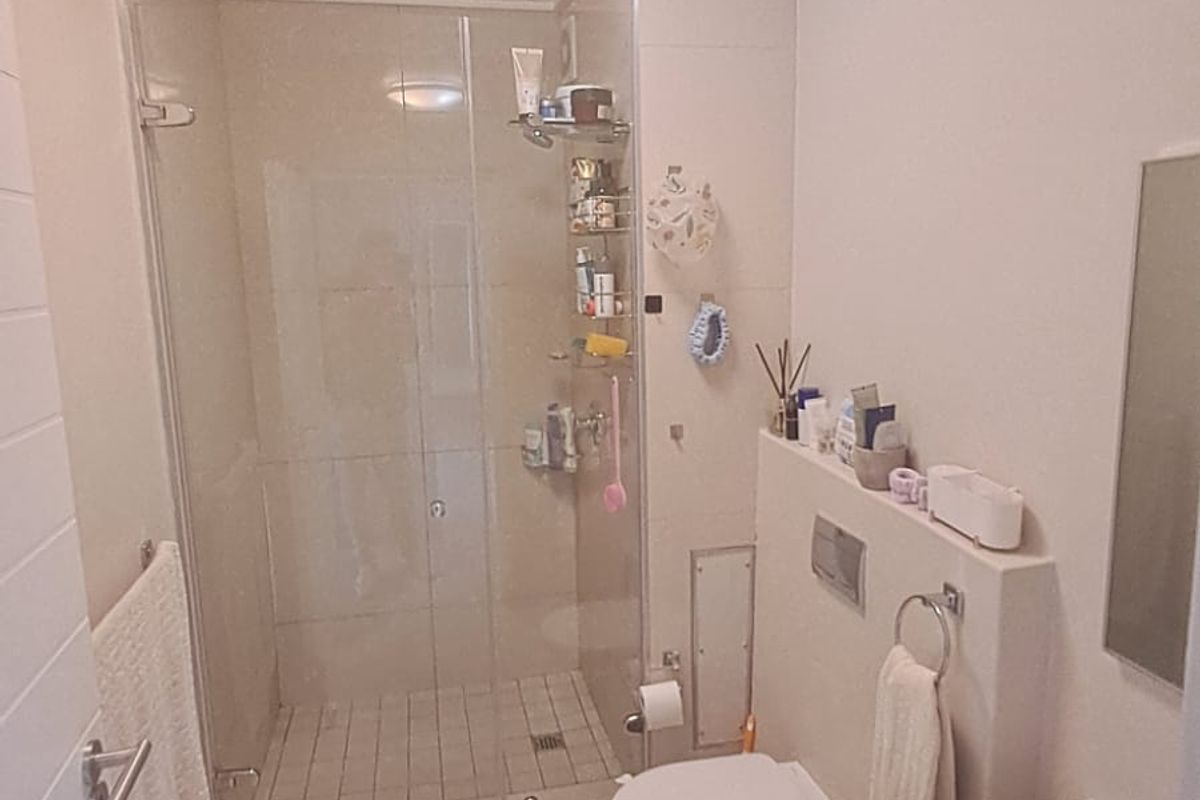 A compact, modern bathroom featuring a glass-enclosed shower, wall-hung toilet, and a vanity basin with neutral tiling throughout.