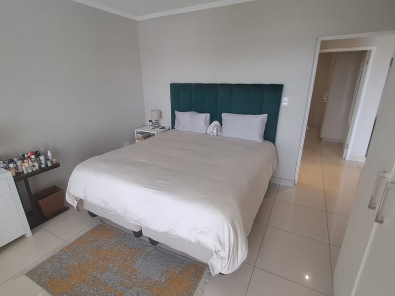 A well-maintained bedroom featuring neutral wall tones, tiled flooring, and a direct view into the adjacent hallway.