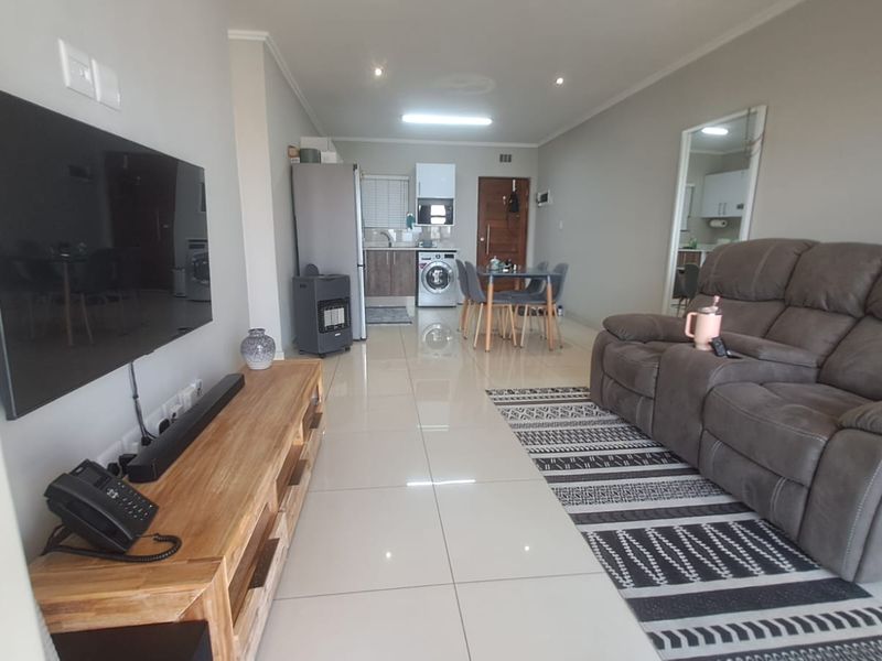 Open-plan living area featuring polished floor tiles, recessed lighting, and a compact kitchen space with integrated laundry facilities.