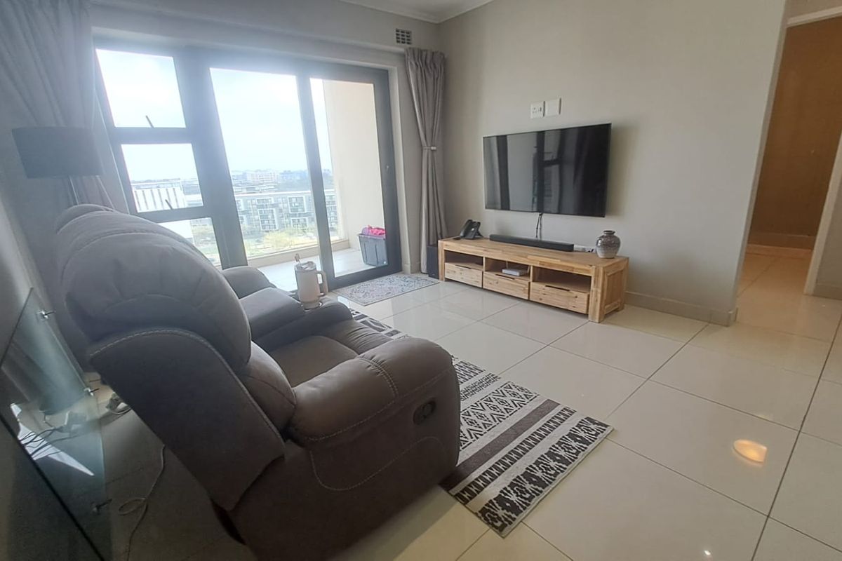 A bright living room featuring large sliding glass doors leading to a balcony, neutral tiled flooring, and recessed ceiling lighting.
