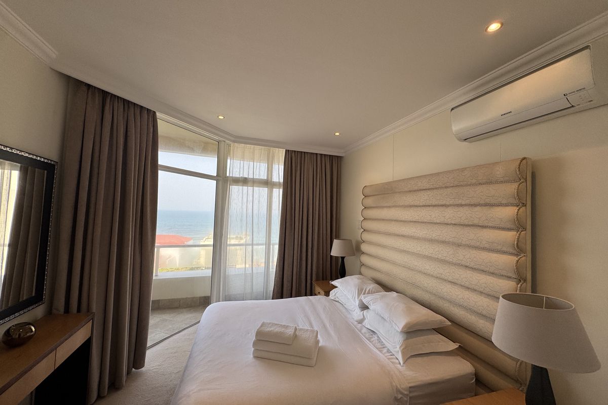 A well-maintained bedroom featuring floor-to-ceiling windows with ocean views, wall-mounted air conditioning, and recessed lighting.
