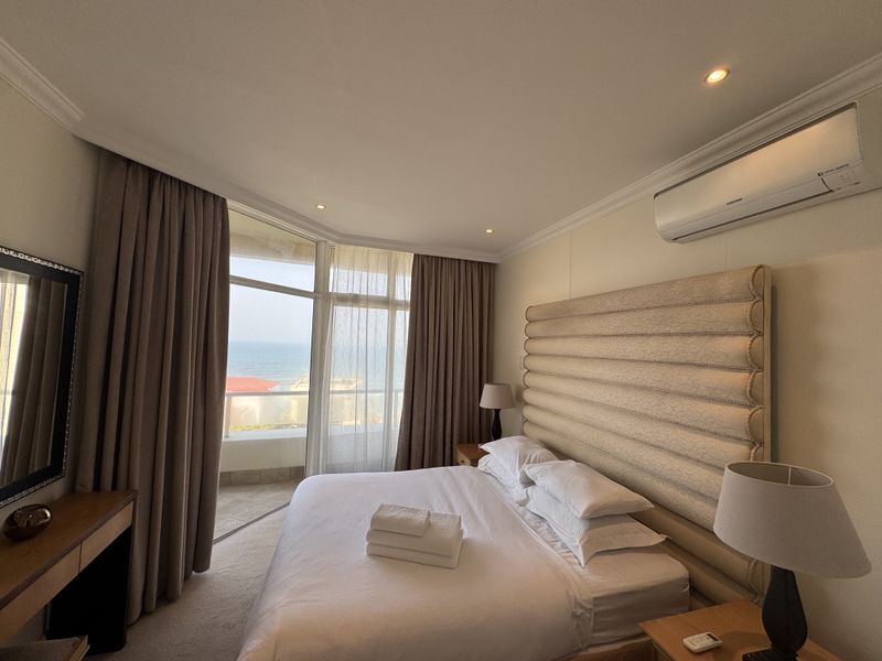 A well-maintained bedroom featuring floor-to-ceiling windows with ocean views, wall-mounted air conditioning, and recessed lighting.