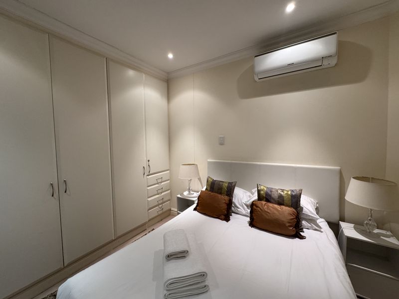 A well-maintained bedroom featuring built-in cupboards, recessed lighting, and a wall-mounted split-system air conditioning unit.