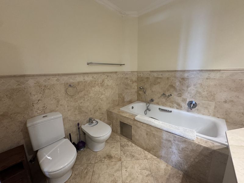 A well-maintained bathroom featuring travertine wall and floor tiles, a built-in bathtub, a bidet, and a standard toilet.
