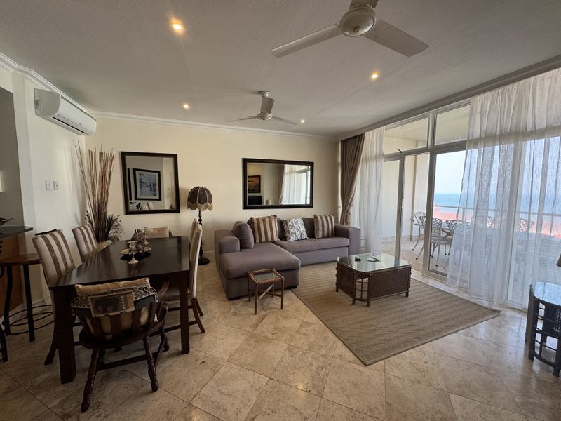 Spacious open-plan living and dining area featuring tiled floors, ceiling fans, and large sliding glass doors leading to a balcony with ocean views.