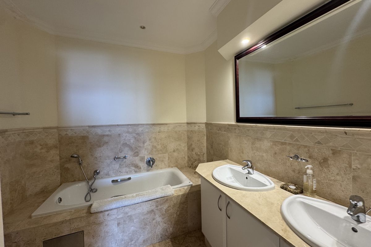 A well-maintained bathroom featuring a double vanity with stone countertops, a built-in bathtub, and neutral stone wall tiling.