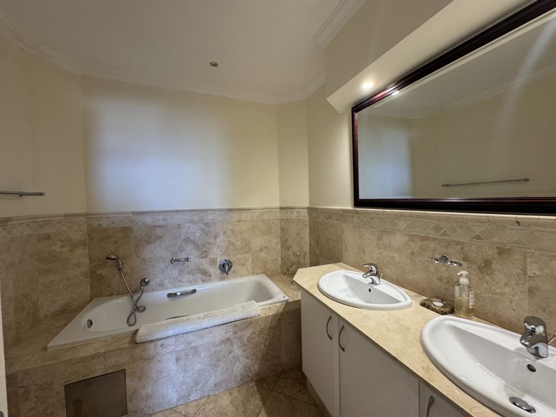 A well-maintained bathroom featuring a double vanity with stone countertops, a built-in bathtub, and neutral stone wall tiling.