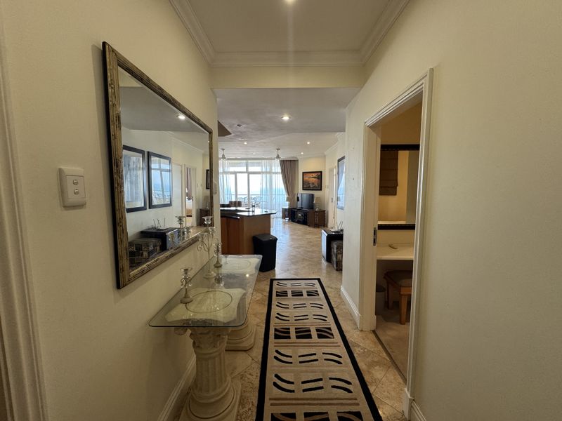 A bright entrance hallway with tiled flooring and crown molding, leading into an open-plan living area with access to a balcony.