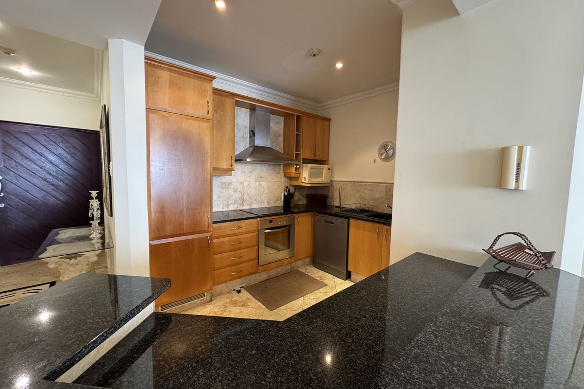 A functional kitchen featuring wooden cabinetry, granite countertops, a breakfast bar, and built-in stainless steel appliances, including an oven and extractor fan.