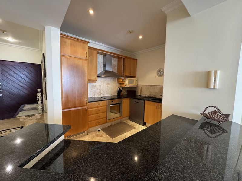 A functional kitchen featuring wooden cabinetry, granite countertops, a breakfast bar, and built-in stainless steel appliances, including an oven and extractor fan.
