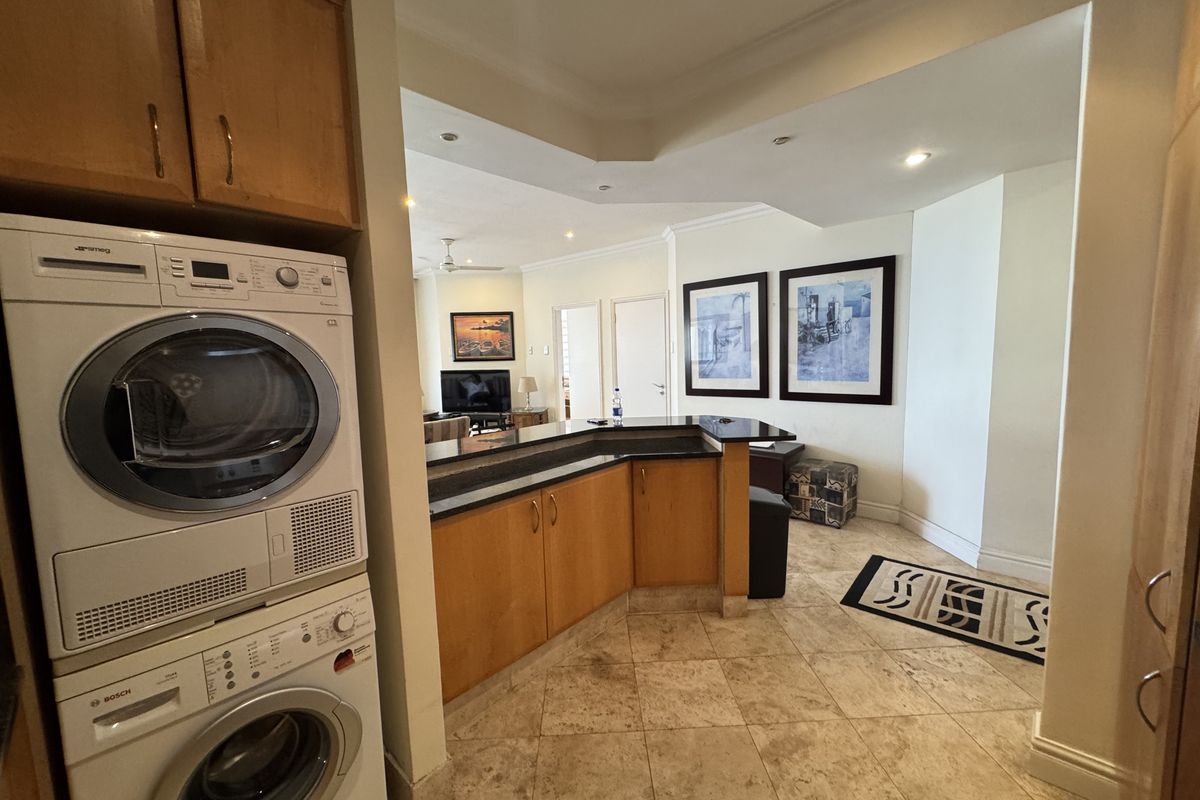 Open plan living area featuring a breakfast bar, tiled flooring, and a dedicated laundry nook with stacked appliances.