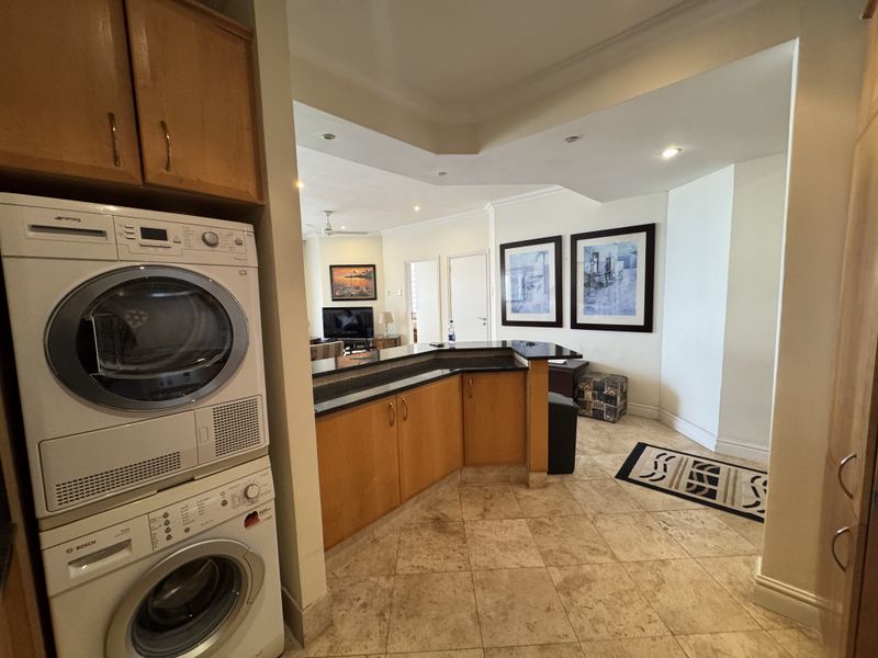 Open plan living area featuring a breakfast bar, tiled flooring, and a dedicated laundry nook with stacked appliances.