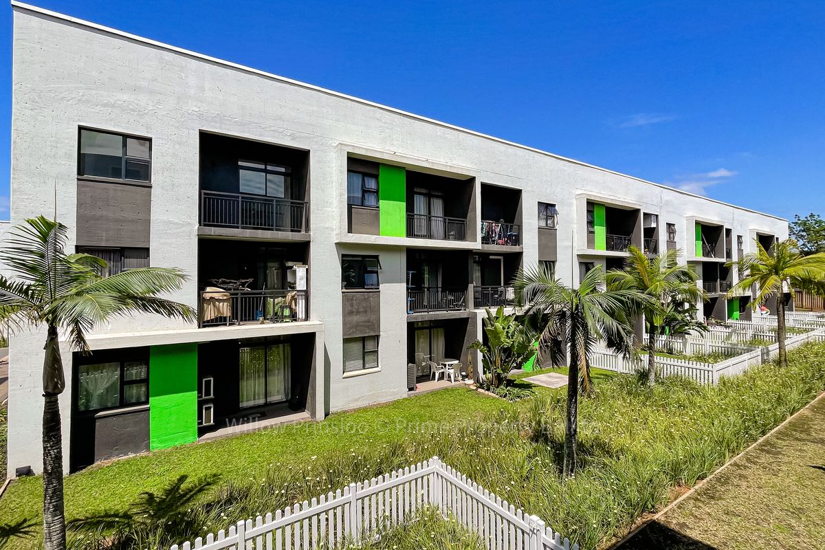 Rear view of a modern apartment complex featuring private balconies, sliding glass doors, and a well-maintained communal garden area with picket fencing.