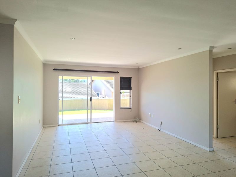 A bright, empty living room featuring neutral tiled flooring, recessed lighting, and a sliding glass door providing access to the outdoor area.