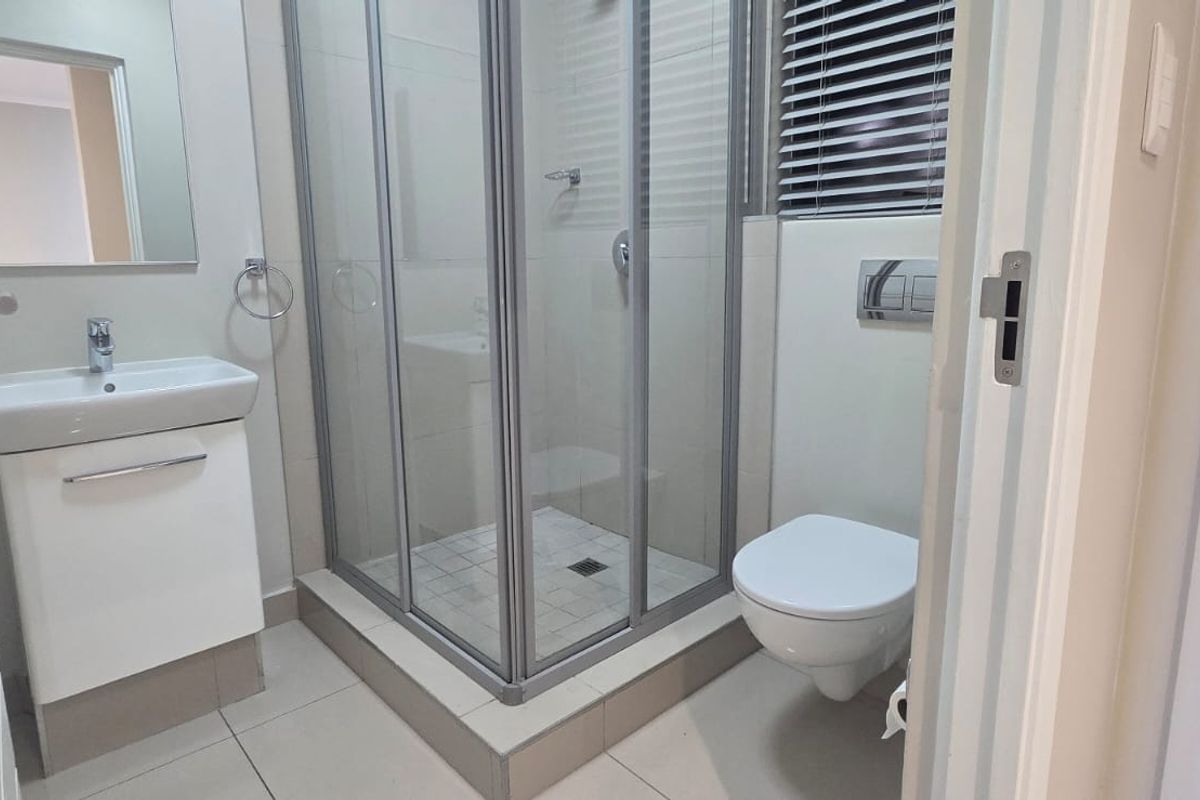 A modern, clean bathroom featuring a glass shower enclosure, wall-mounted toilet, and a vanity basin with a mirror.