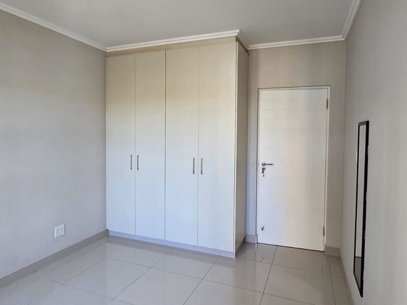 A clean, empty bedroom featuring neutral walls, tiled flooring, and a built-in wardrobe with ample storage space.