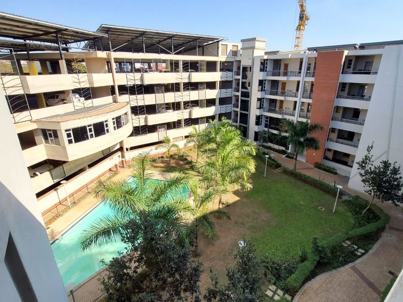 Elevated view of the apartment complex courtyard featuring a swimming pool, landscaped garden, and multi-level parking structure.