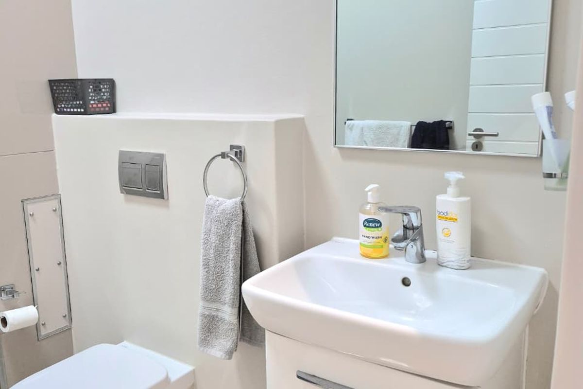 A clean and modern bathroom featuring a wall-hung toilet with a concealed cistern, a vanity basin with storage, and a wall-mounted mirror.