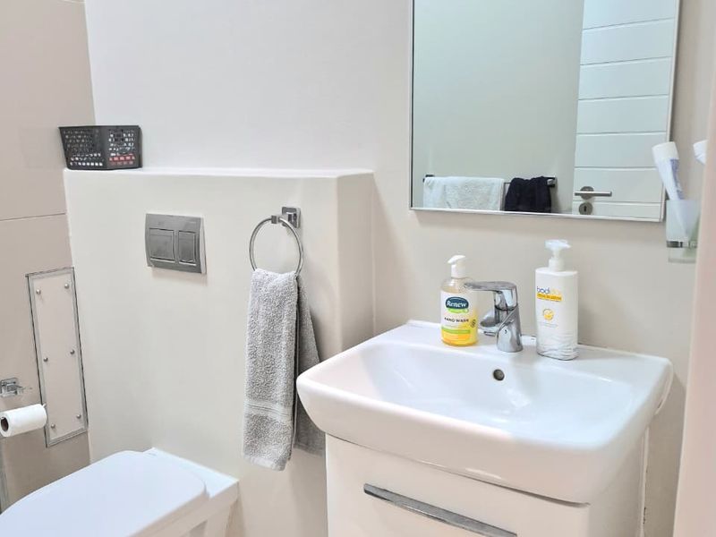 A clean and modern bathroom featuring a wall-hung toilet with a concealed cistern, a vanity basin with storage, and a wall-mounted mirror.