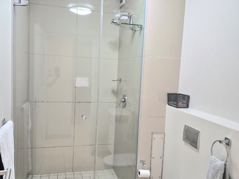 Modern bathroom featuring a glass-enclosed shower with tiled flooring and a wall-mounted toilet with a concealed cistern.