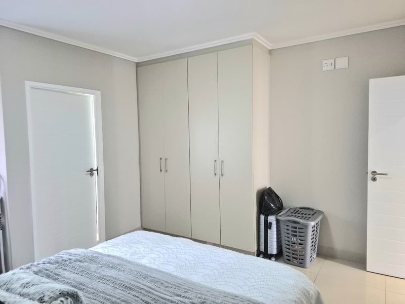 A clean bedroom featuring neutral walls, tiled flooring, and ample built-in cupboard storage with modern finishes.