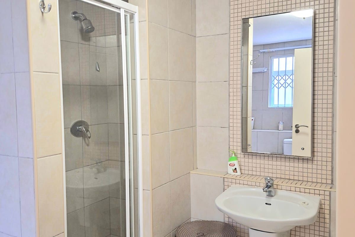 A functional bathroom featuring a shower enclosure, wall-mounted basin, and neutral tiled finishes throughout.