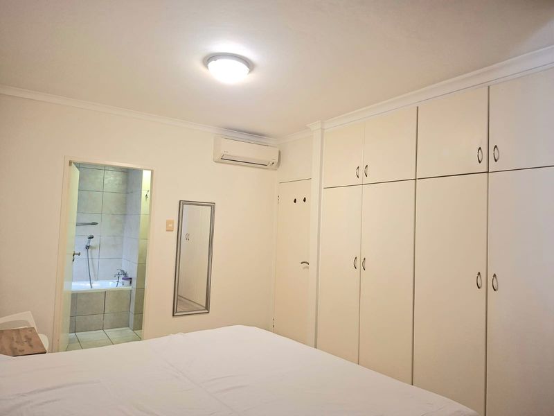 A well-maintained bedroom featuring extensive built-in cabinetry, a split-system air conditioner, and direct access to an en-suite bathroom.