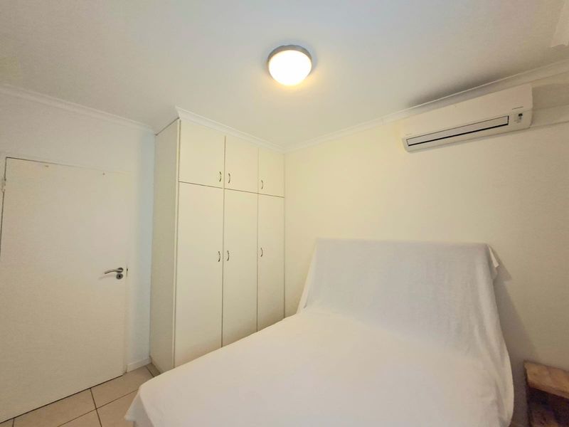 A clean bedroom featuring built-in cupboards, tiled flooring, and a wall-mounted split-system air conditioner.