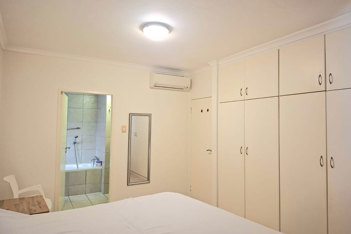 A well-maintained bedroom featuring extensive built-in cabinetry, a split-system air conditioner, and direct access to an en-suite bathroom.