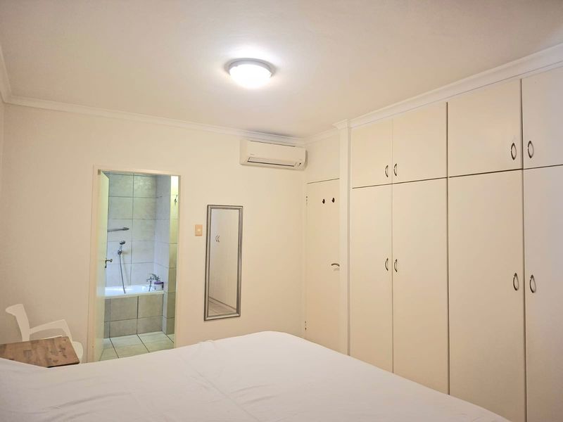 A well-maintained bedroom featuring extensive built-in cabinetry, a split-system air conditioner, and direct access to an en-suite bathroom.