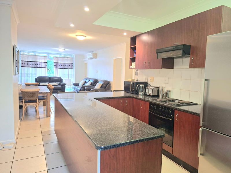 Open-plan living area featuring a kitchen with granite countertops, built-in cabinetry, and integrated appliances, flowing into a spacious dining and lounge area.