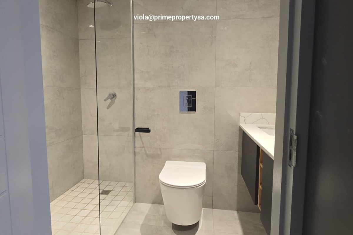Modern bathroom featuring a walk-in shower with glass screen, wall-mounted toilet, and a sleek vanity with stone countertop.