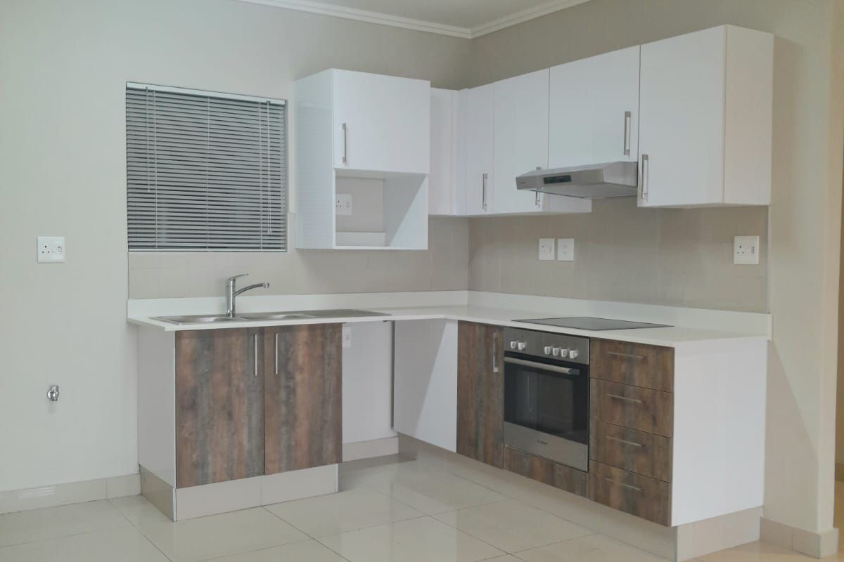 Modern kitchen featuring two-tone cabinetry, built-in oven, electric hob, extractor fan, stainless steel sink, and neutral tiled flooring.