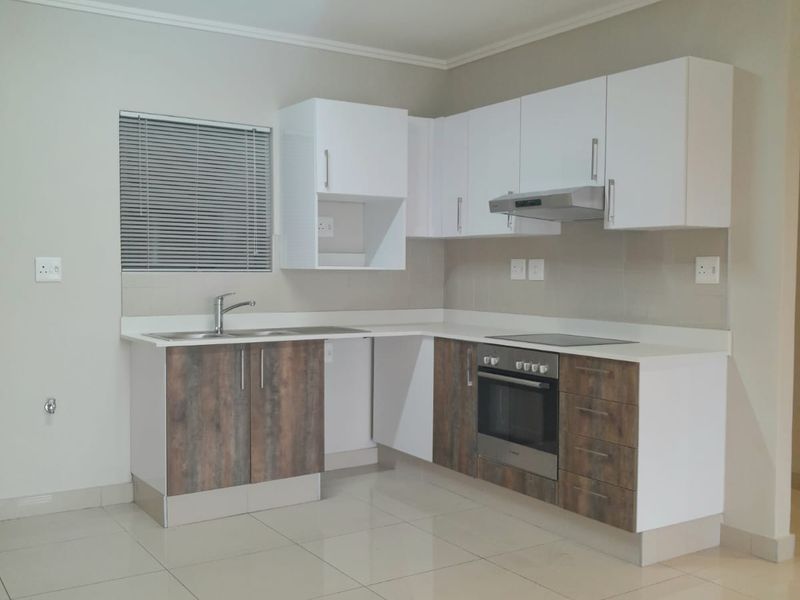 Modern kitchen featuring two-tone cabinetry, built-in oven, electric hob, extractor fan, stainless steel sink, and neutral tiled flooring.