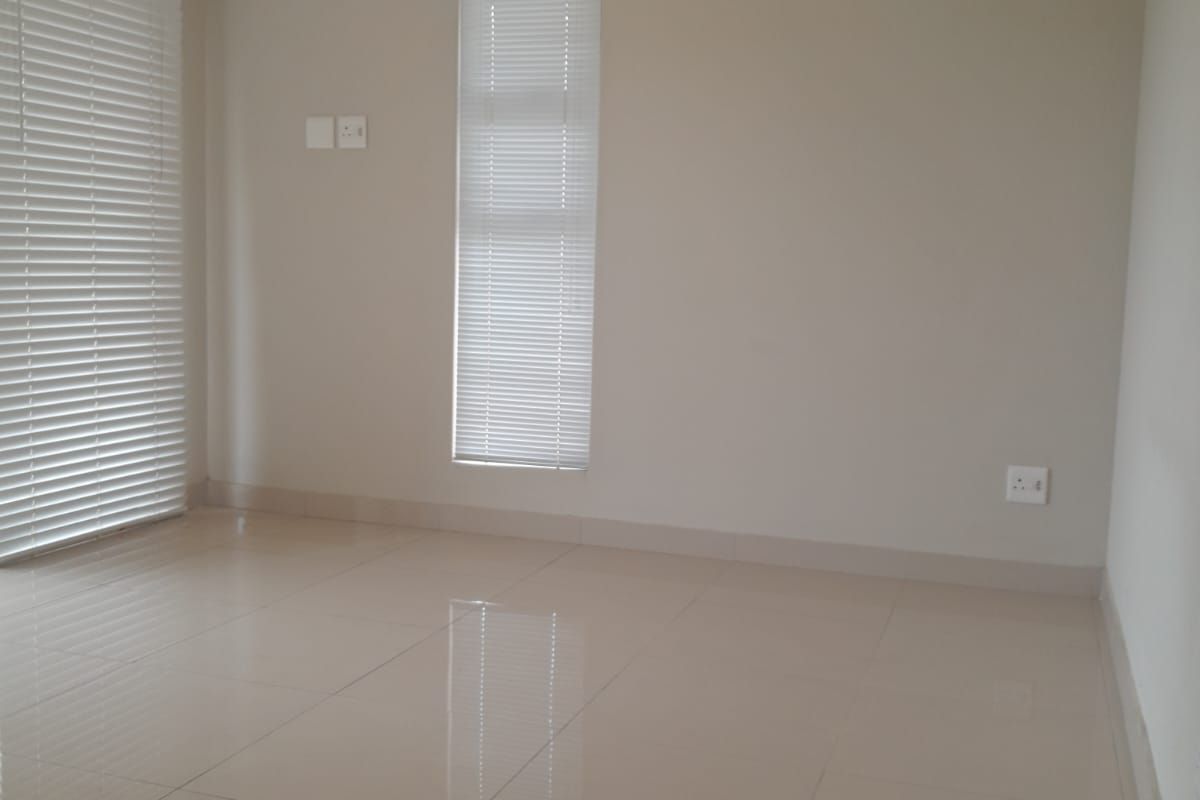 A bright, empty living area featuring neutral tiled flooring, clean walls, and fitted venetian blinds, offering a versatile space ready for furnishing.