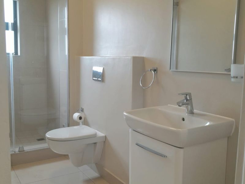 Modern bathroom featuring a wall-mounted toilet, vanity basin with mixer tap, and a glass-enclosed shower with neutral tiled flooring.