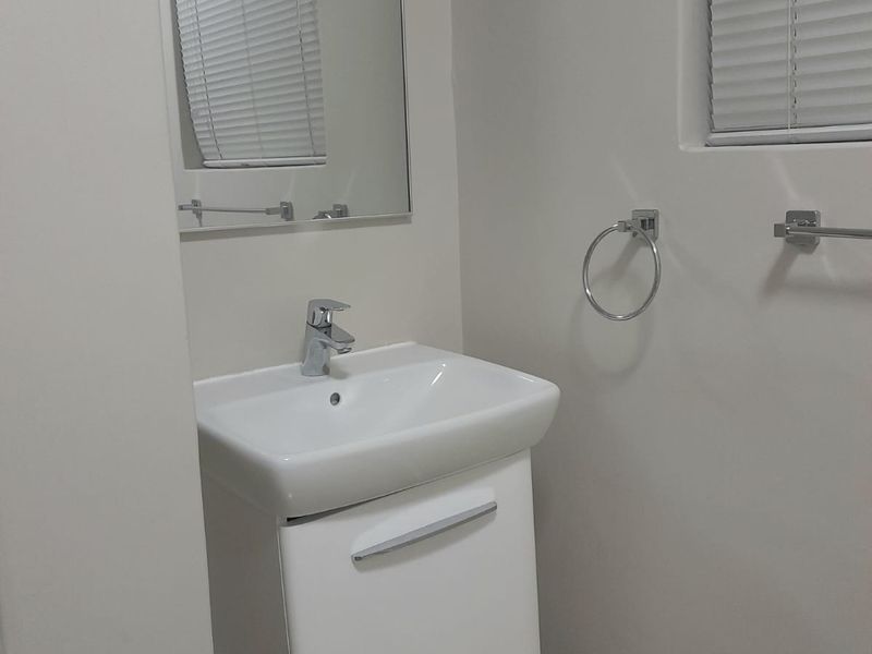 A clean and modern bathroom featuring a white vanity cabinet with a basin, mixer tap, wall mirror, and chrome towel fixtures.