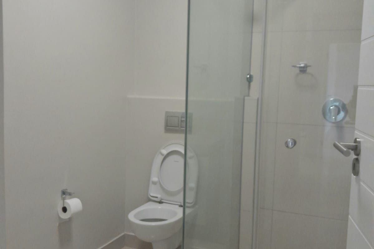 A clean, modern bathroom featuring a wall-mounted toilet, a glass-enclosed shower, and neutral floor tiling.