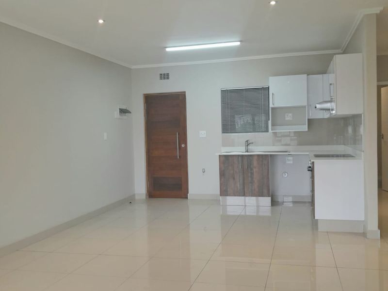 An open-plan living and kitchen area featuring neutral tiled flooring, modern cabinetry, and recessed lighting in a clean, vacant space.