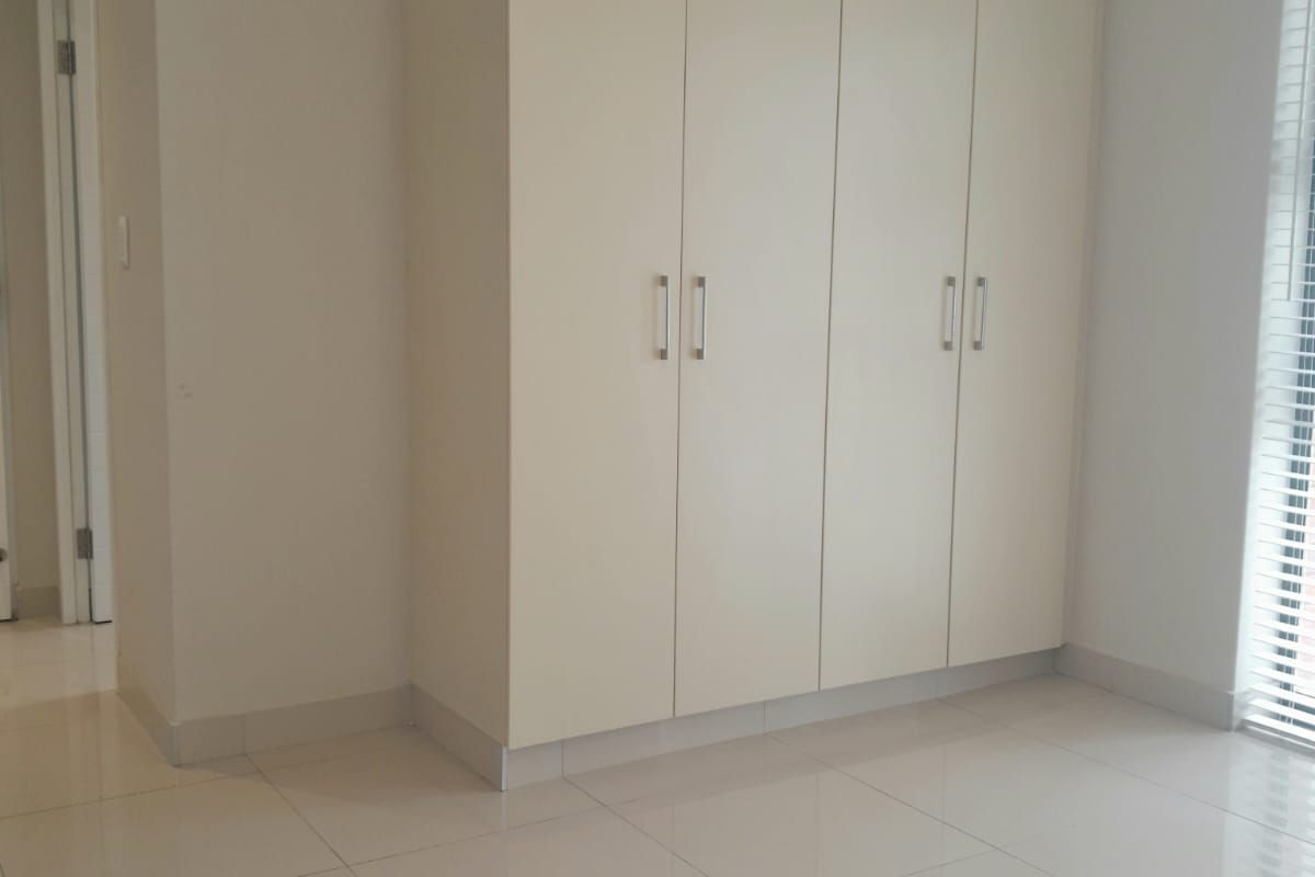 A bright, empty bedroom featuring neutral tiled flooring, built-in floor-to-ceiling cupboards, and venetian blinds, offering a clean and versatile living space.