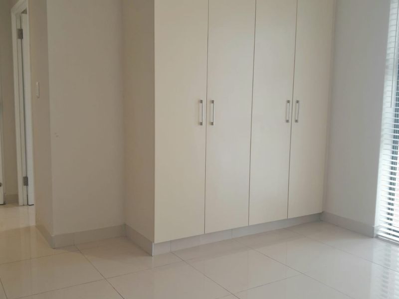 A bright, empty bedroom featuring neutral tiled flooring, built-in floor-to-ceiling cupboards, and venetian blinds, offering a clean and versatile living space.