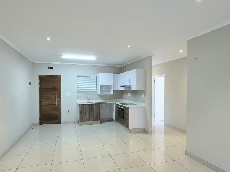 An open-plan living and kitchen area featuring tiled flooring, modern built-in cabinetry, integrated appliances, and recessed lighting in a clean, vacant space.
