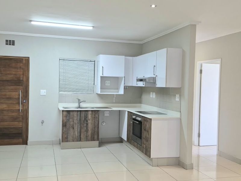 An open-plan kitchen area featuring modern two-tone cabinetry, built-in oven and hob, tiled flooring, and recessed lighting in a clean, neutral space.