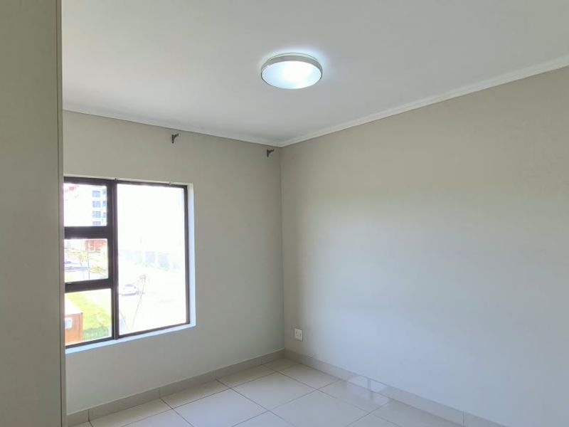 A clean, empty bedroom featuring neutral wall tones, tiled flooring, and a large window providing natural light.