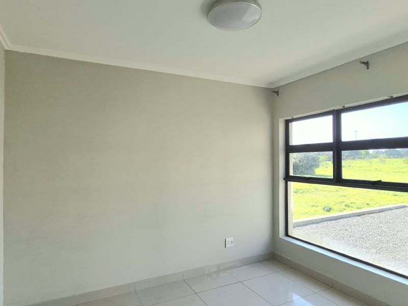 A bright, empty bedroom featuring neutral tiled flooring and large windows that provide ample natural light and pleasant outdoor views.