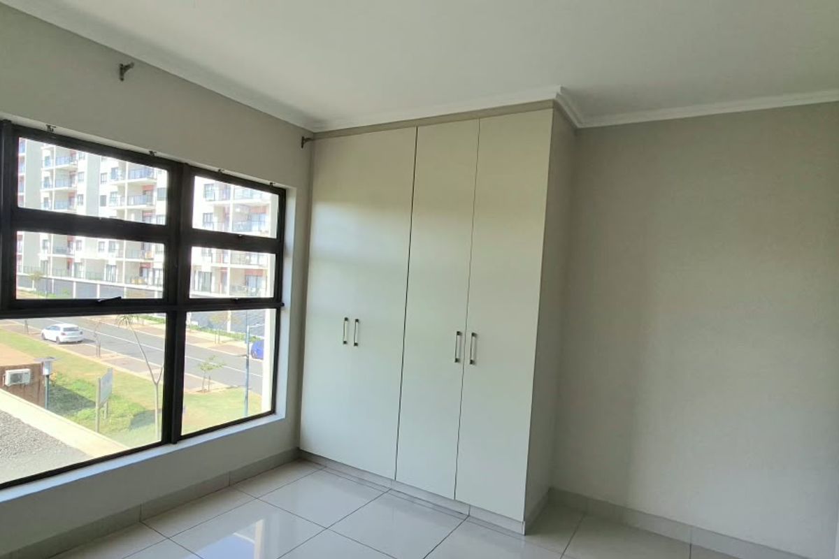A bright, empty bedroom featuring large windows, neutral tiled flooring, and built-in cupboards, offering a clean and well-maintained space.
