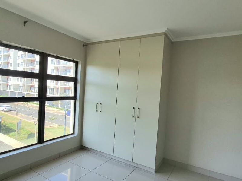 A bright, empty bedroom featuring large windows, neutral tiled flooring, and built-in cupboards, offering a clean and well-maintained space.